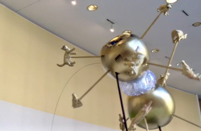 A statue of a golden space probe with prongs jutting out of it with toy cats on the end of each prong